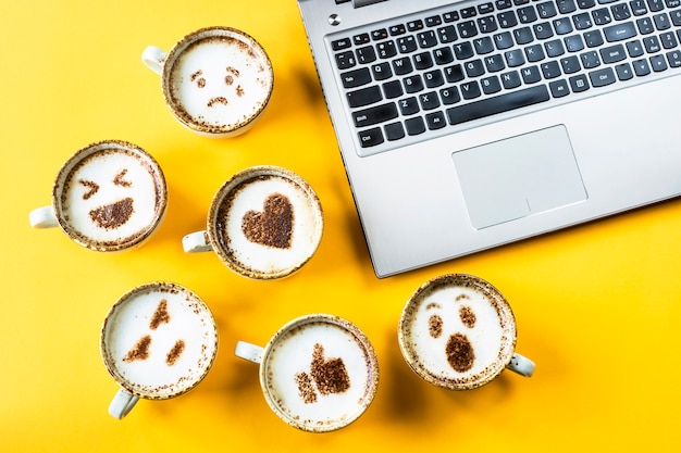 Smile emoji peint sur des tasses de cappuccino à côté de l&#39;ordinateur portable