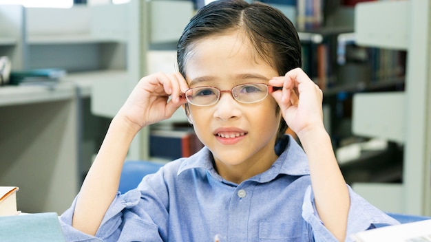 Smiley drôle mignon garçon assis et maintenez les lunettes sur le visage avec le livre