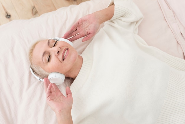 Smiley femme mûre appréciant la musique sur les écouteurs au lit