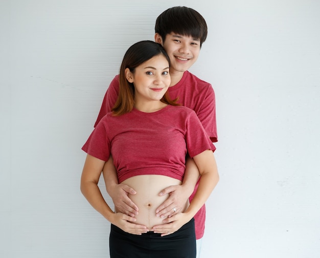 Smiley jeune mari et femme debout ensemble sur fond blanc. Un homme embrasse une femme enceinte en posant sa main sur son ventre. Concept de personnes, de famille et de style de vie. Espace de copie.