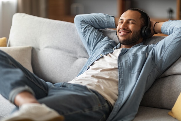 Smiling African American Guy écoute de la musique tout en vous relaxant sur le canapé à la maison