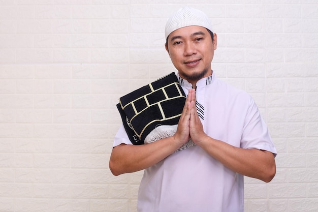 Smiling Asian Muslim man gesturing Eid Mubarak salutation isolé sur fond blanc