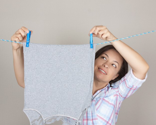 Smiling Attractive Woman Hanging chiffon propre et humide à sécher sur une corde à linge à la buanderie sur un fond gris