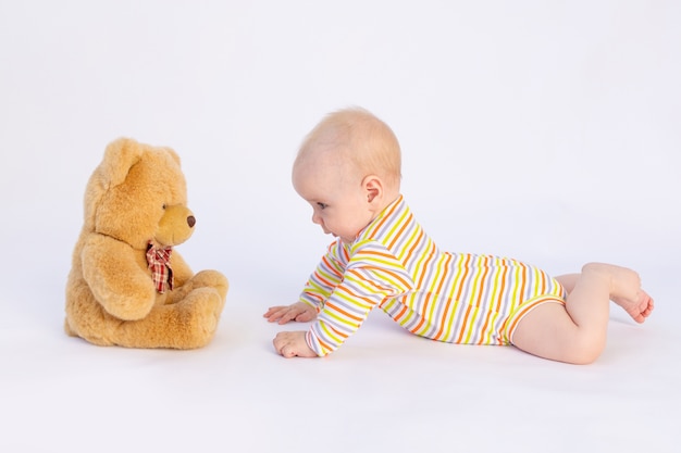 Smiling baby girl 6 mois se trouve dans un body lumineux devant un ours en peluche doux,