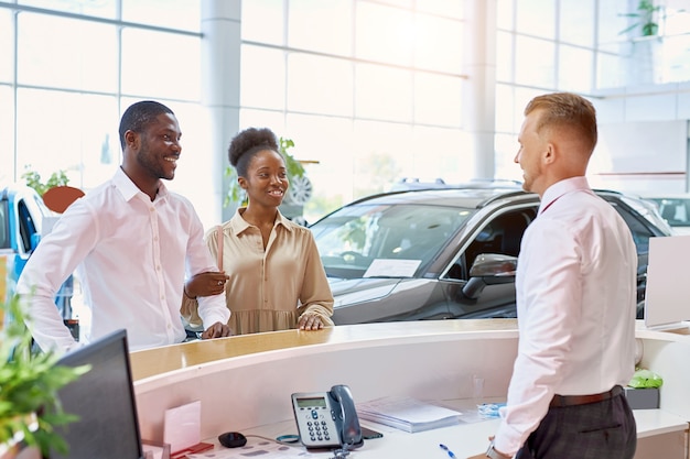 Photo smiling caucasian sales expert accueillant les clients dans la salle d'exposition de voiture