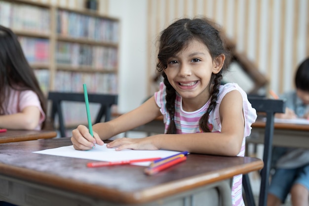 Smiling cute kid girl dessin au crayon de couleur sur papier blanc en classe d'art à l'école élémentaire