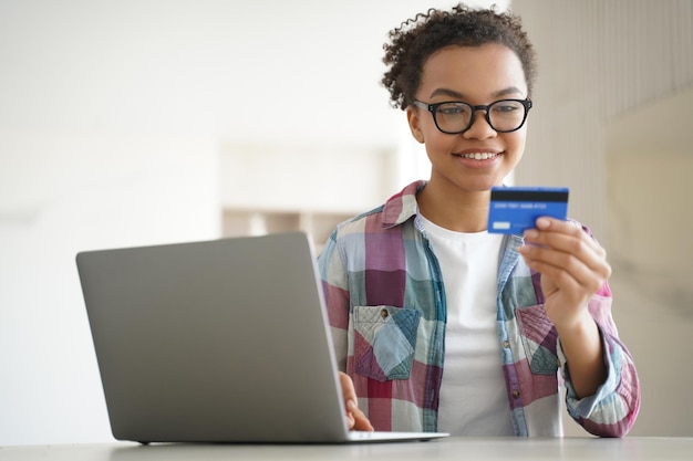 Smiling mixed race young girl holding carte de crédit utilise des services bancaires en ligne sur ordinateur portable