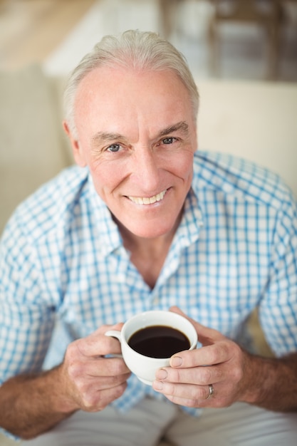 Smiling senior man ayant une tasse de café dans le salon