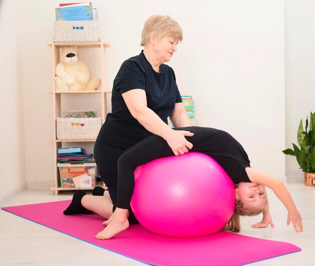 Smiling senior woman doing stretching exercices backbend sur fit ball avec sa petite-fille