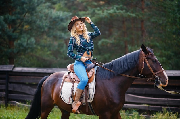 Smilng jolie jeune cow-girl Une femme de style cow-boy dans une chemise à carreaux assis sur un cheval et tenant un chapeau de cow-boy