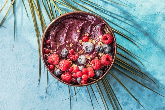 Smoothie d'açai surgelé en coque de noix de coco avec framboises, banane, myrtilles, fruits et granola sur fond de béton. Petit-déjeuner, repas sain pour les vibrations estivales, vue de dessus, espace pour le texte