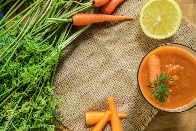 Smoothie aux carottes fraîches en verre sur fond en bois rustique.