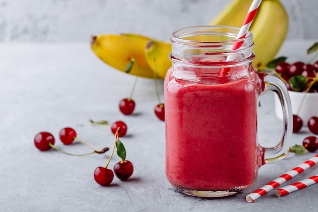 Smoothie aux cerises et à la banane dans un bocal en verre avec de la paille