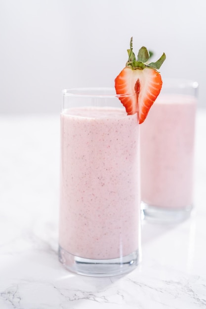 Smoothie aux fraises et aux bananes pour le petit-déjeuner sain fraîchement préparé, garni de fraises fraîches et de paille en papier.