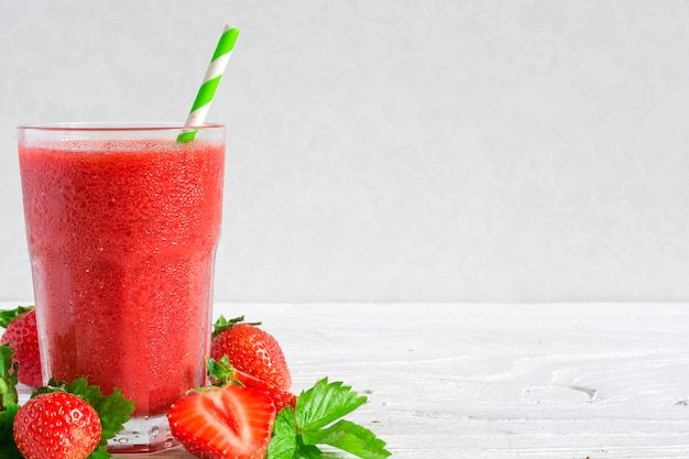 Smoothie aux fraises dans un verre avec de la paille et des baies fraîches