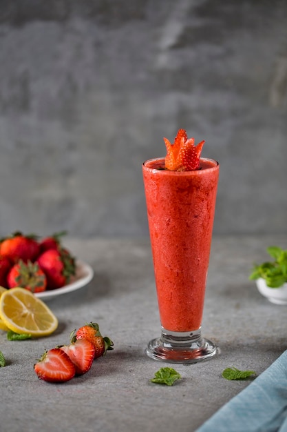 Smoothie aux fraises fraîches avec fraise crue et tranche de citron vert servi dans une vue latérale en verre sur fond gris