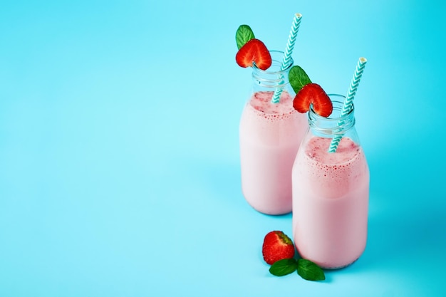 Smoothie aux fraises ou milkshake dans un bocal en verre avec des baies sur fond bleu boisson d'été saine