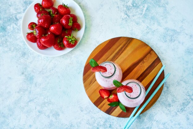 Photo smoothie aux fraises ou milkshake dans un pot en verre avec des baies sur fond de béton bleu