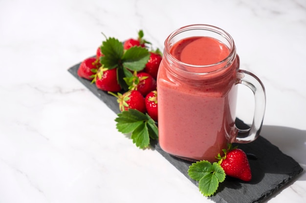 Smoothie aux fraises ou milkshake sur un plat en ardoise avec des fraises fraîches et des feuilles vertes sur fond de marbre Recette de boisson aux fraises dans une tasse pleine de vitamines et d'antioxydants