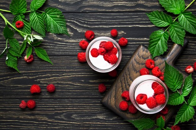 Smoothie aux framboises dans des bocaux en verre avec baies fraîches et yaourt sur fond de table de cuisine en bois vintage vue de dessus à plat