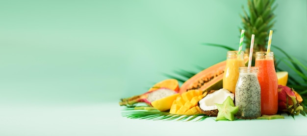 Smoothie aux fruits juteux papaye et ananas mangue orange dans des bocaux sur fond turquoise Detox été régime alimentaire concept végétalien bannière espace copie jus frais dans des bouteilles en verre sur des feuilles de palmier