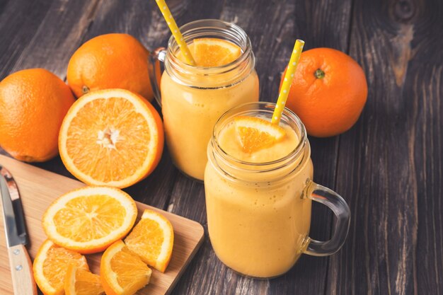 Smoothie aux fruits à l'orange dans les bocaux en verre avec des tranches d'orange fraîches sur fond de bois rustique. Photo aux tons vintage.