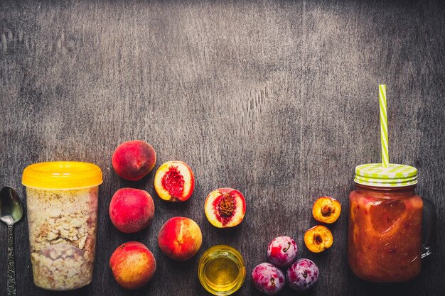 Smoothie aux fruits de pêche utile dans une bouteille en verre et des pailles et des flocons d'avoine avec des petits déjeuners végétariens aux fruits