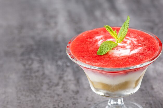 Smoothie aux fruits avec un pétale dans un vase en verre sur une surface grise.