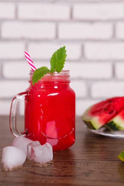 Smoothie aux fruits rouges mélangé dans un bocal en verre avec de la paille et des morceaux de glace. Tranches de melon d'eau sur une assiette. Mise au point sélective. Récolte .