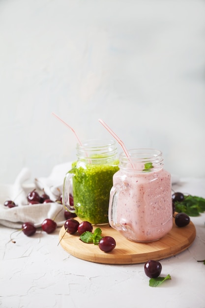 Smoothie aux herbes fraîches et smoothie aux cerises dans des bocaux en verre sur un support en bois