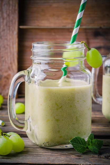 Smoothie aux raisins détox bio vert dans un bocal en verre sur fond rustique en bois