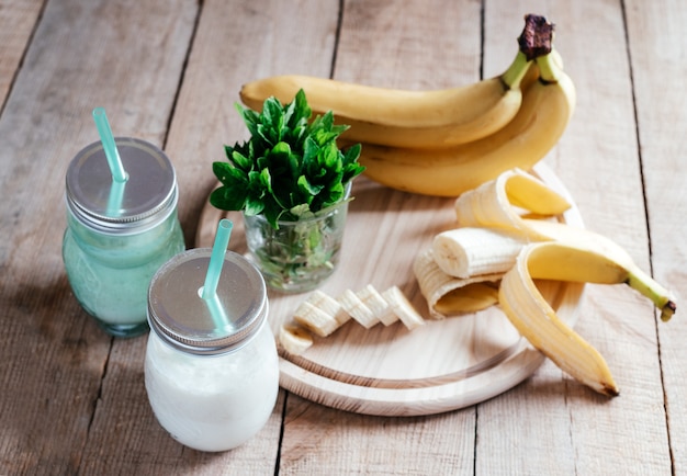 Smoothie à la banane d'été ou milk-shake à la menthe et à la paille dans des bocaux sur une table en bois foncé avec espace de copie