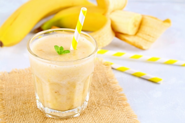 Smoothie à la banane avec un tube en papier et à la menthe. Les bananes sont entières et coupées sur un fond gris.