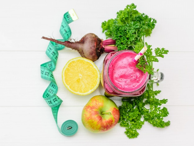 Smoothie De Betteraves Fraîches, Citron, Pomme, Ruban à Mesurer Et Persil Sur Une Table En Bois Blanc.