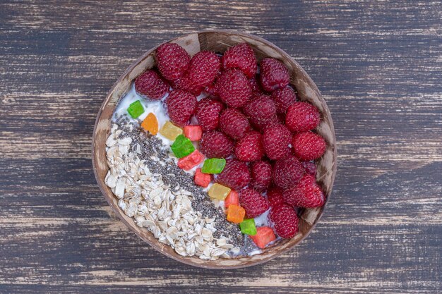 Smoothie dans un bol de noix de coco avec des framboises, des flocons d'avoine, des fruits confits et des graines de chia pour le petit-déjeuner en gros plan Le concept d'une alimentation saine superfood