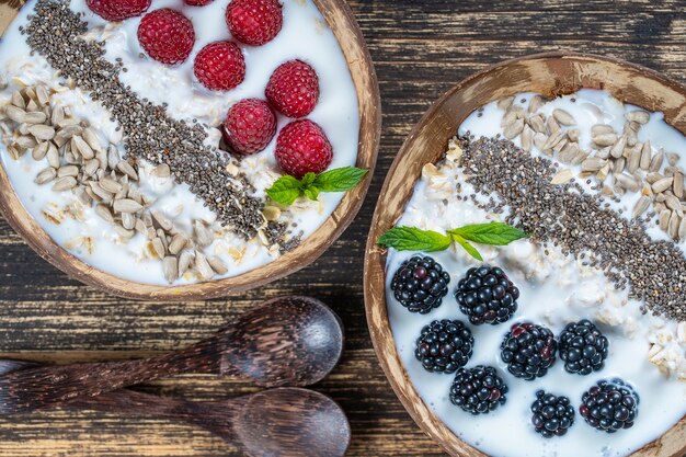 Smoothie dans un bol de noix de coco avec mûres, framboises, flocons d'avoine, graines de tournesol et graines de chia pour le petit-déjeuner, gros plan. Le concept d'une alimentation saine, superaliments. Vue de dessus