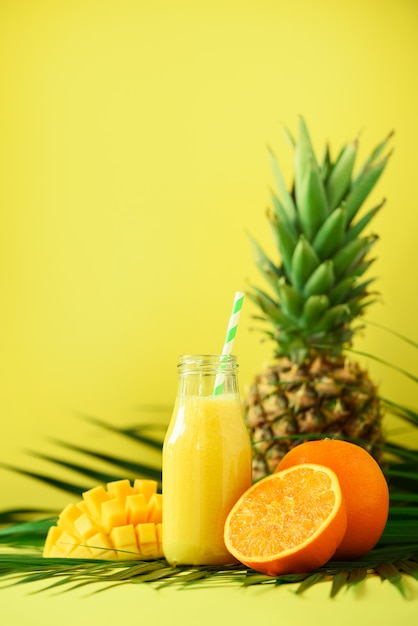 Smoothie délicieux juteux avec fruits orange, mangue, ananas. Jus de fruits frais dans un bocal en verre sur des feuilles de palmier vert.