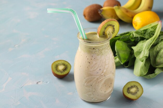 Smoothie détox sain kiwi, banane, épinards et citron dans un bocal en verre sur fond bleu clair avec des ingrédients frais