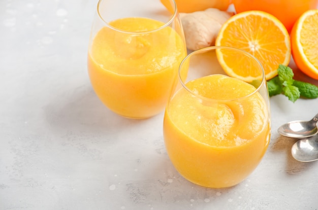 Smoothie frais avec kaki, orange et gingembre sur fond de béton gris.