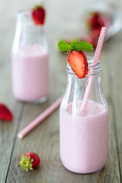 Smoothie fraise en bonne santé, milk-shake, dans des bouteilles traditionnelles avec fraises et paille rose