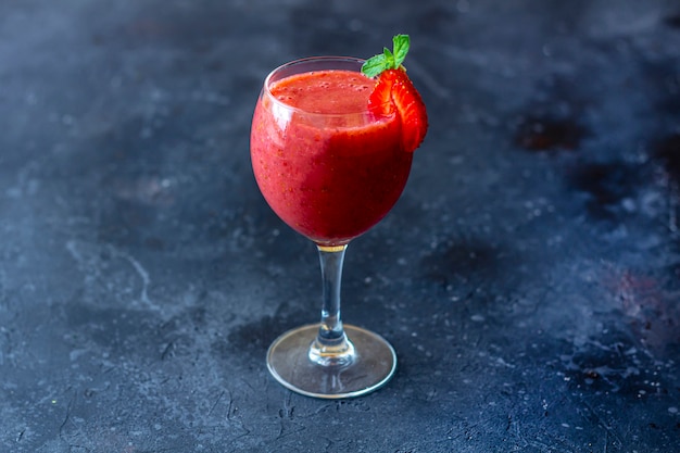 Smoothie fraise glacée fraîche dans un verre à vin décoré d'une tranche de fraise et de menthe sur fond sombre. Boisson Slushy d'été.