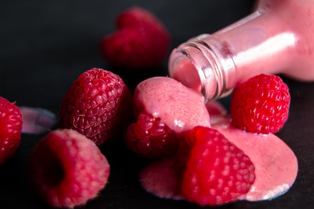 Smoothie framboise renversé de la bouteille sur un tableau noir près de baies.