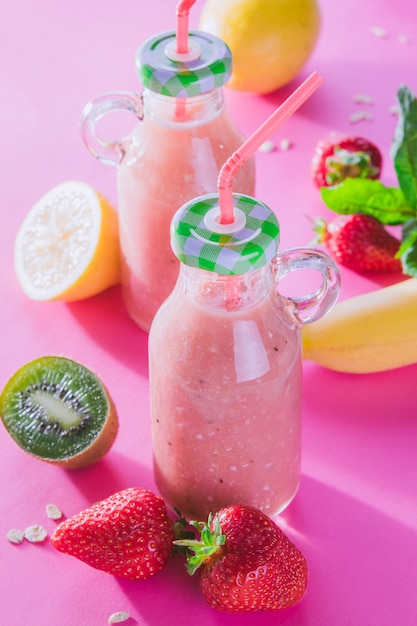 Smoothie fruité dans des bouteilles en verre avec des ingrédients sur fond rose