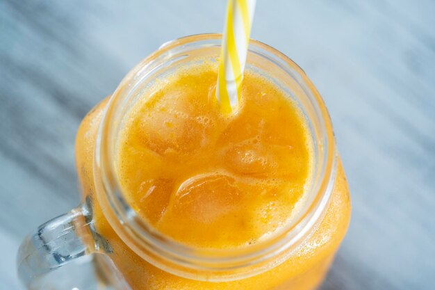 Smoothie jaune bio frais dans une tasse en verre sur une table en bois blanc gros plan Boisson aux fruits d'été rafraîchissante Le concept d'une alimentation saine Smoothie à l'argousier