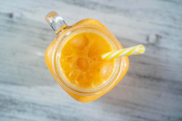 Smoothie jaune bio frais dans une tasse en verre sur une table en bois blanc gros plan Boisson aux fruits d'été rafraîchissante Le concept d'une alimentation saine Smoothie à l'argousier