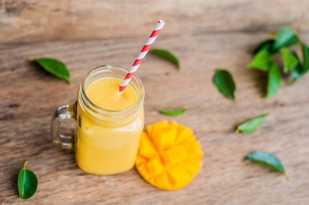 Smoothie juteux de mangue dans un bocal en verre avec de la paille rouge à rayures sur fond de bois ancien