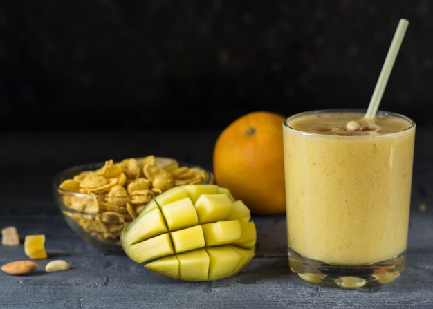 Un smoothie de mangue, banane, céréales et miel sur la table en bois sombre dans un bécher en verre