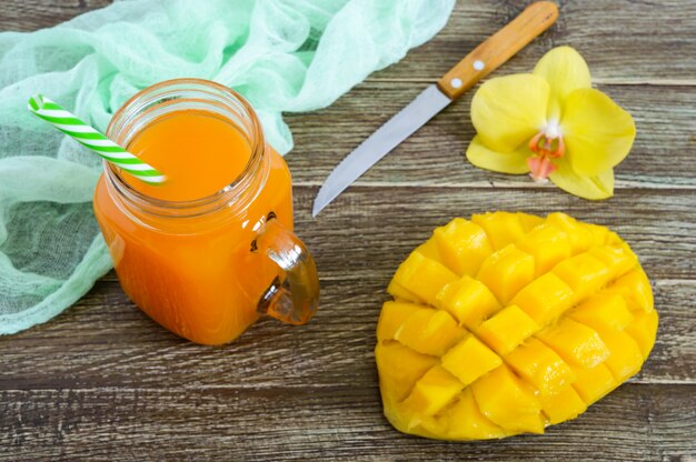 Photo smoothie à la mangue dans un bocal en verre et mangue fraîche sur un fond en bois. shake à la mangue. concept de fruits tropicaux.