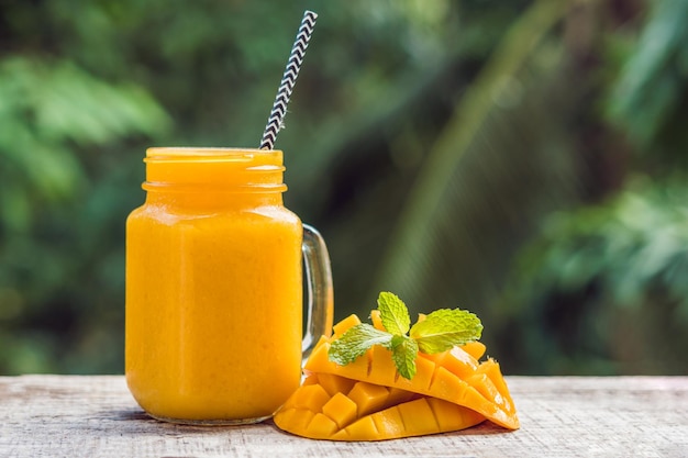 Smoothie à la mangue dans un pot Mason en verre et mangue sur fond vert. Shake à la mangue. Notion de fruits tropicaux