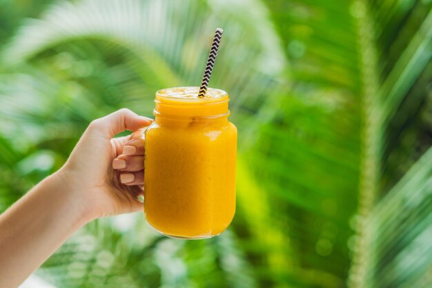 Smoothie à la mangue dans un pot Mason en verre et mangue sur fond vert. Shake à la mangue. Notion de fruits tropicaux